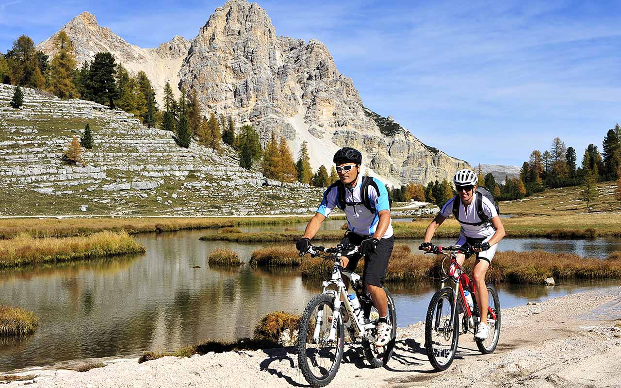 Cyclists ride along a mountain lake on the Alpe di Fanes